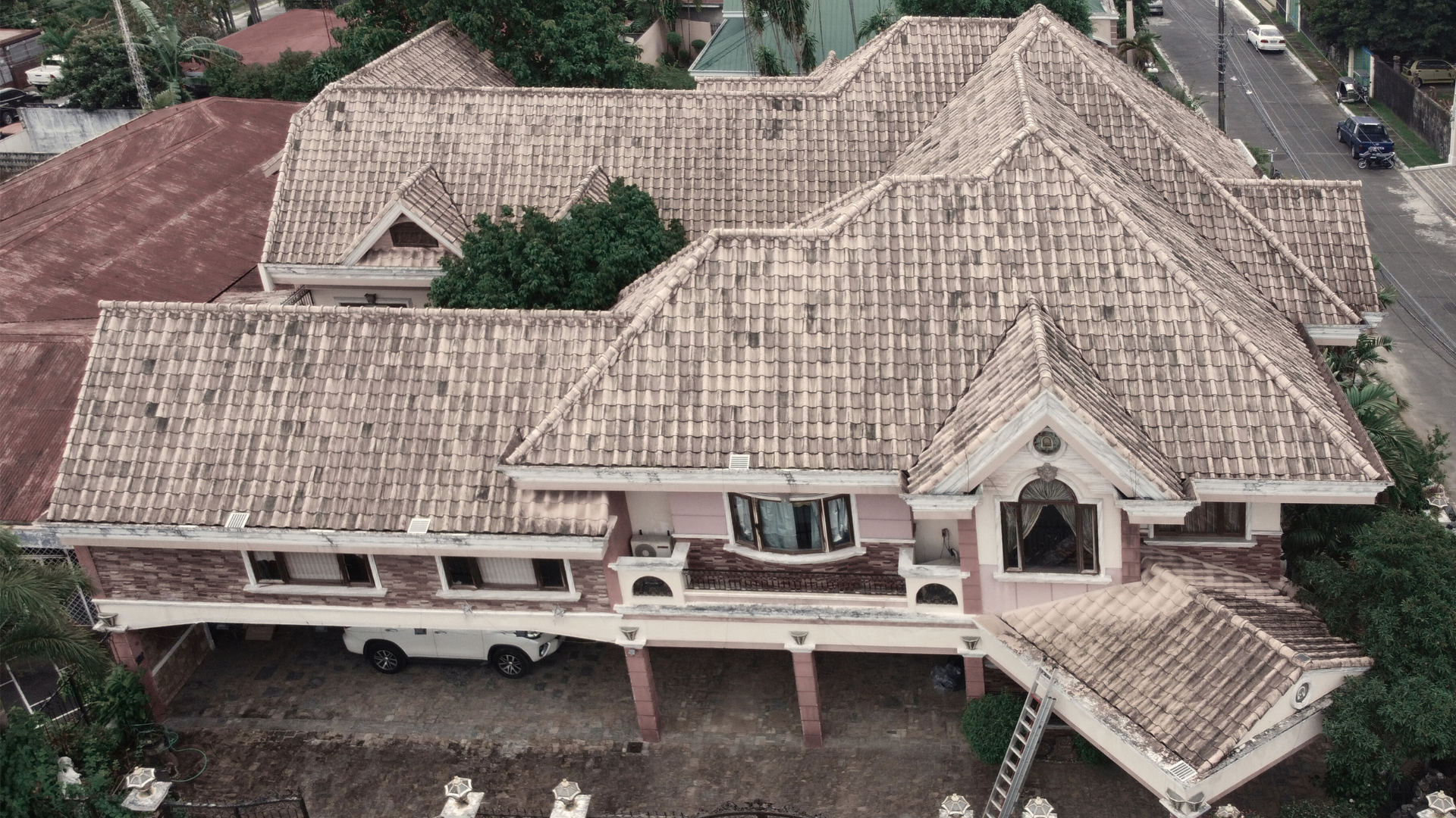 Aerial drone view of a large residential home with terracotta roof tiles covered in black algae and moss buildup before softwashing.
