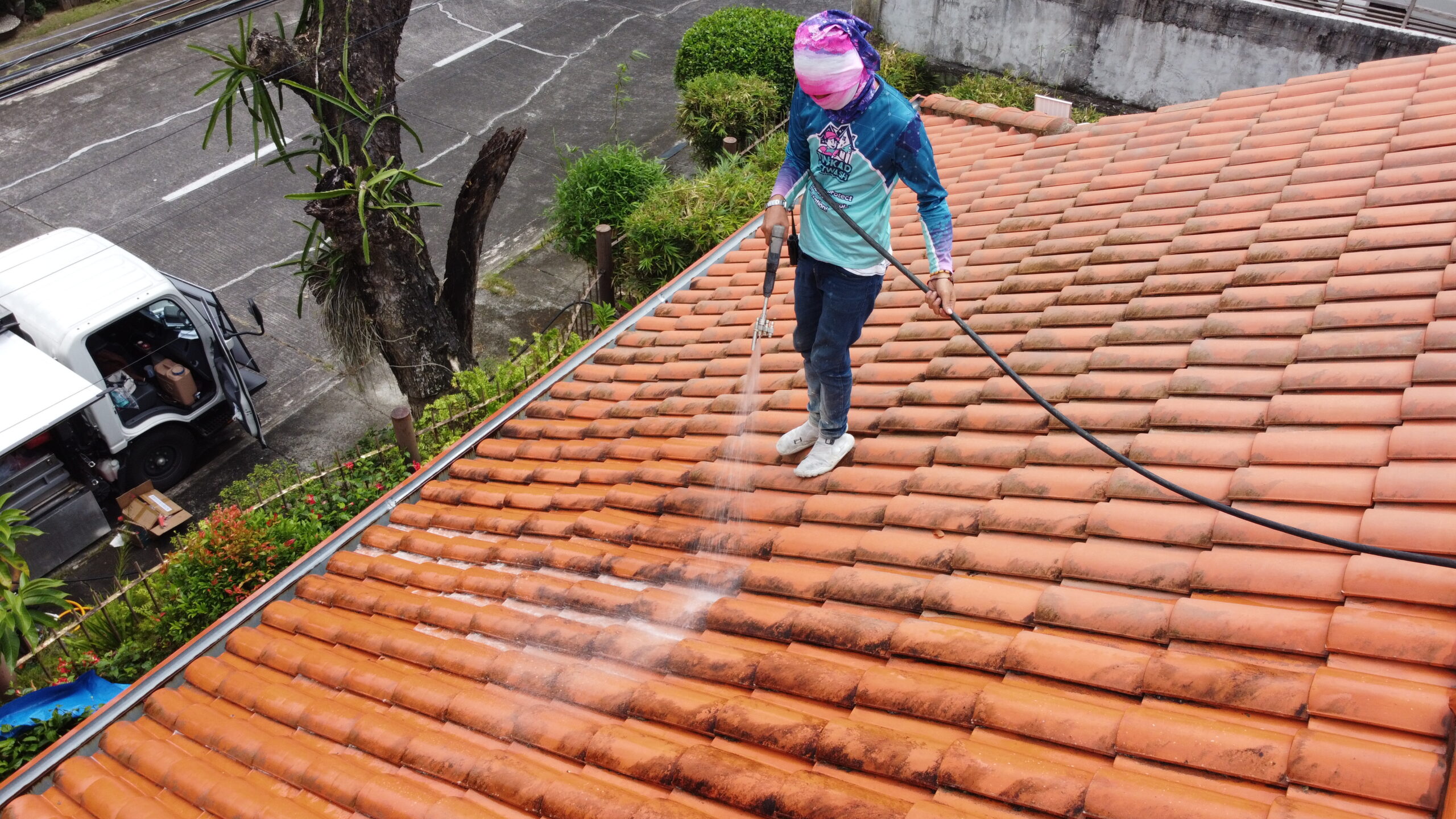 Professional roof cleaning service pressure washing terracotta clay tiles to remove dark stains.