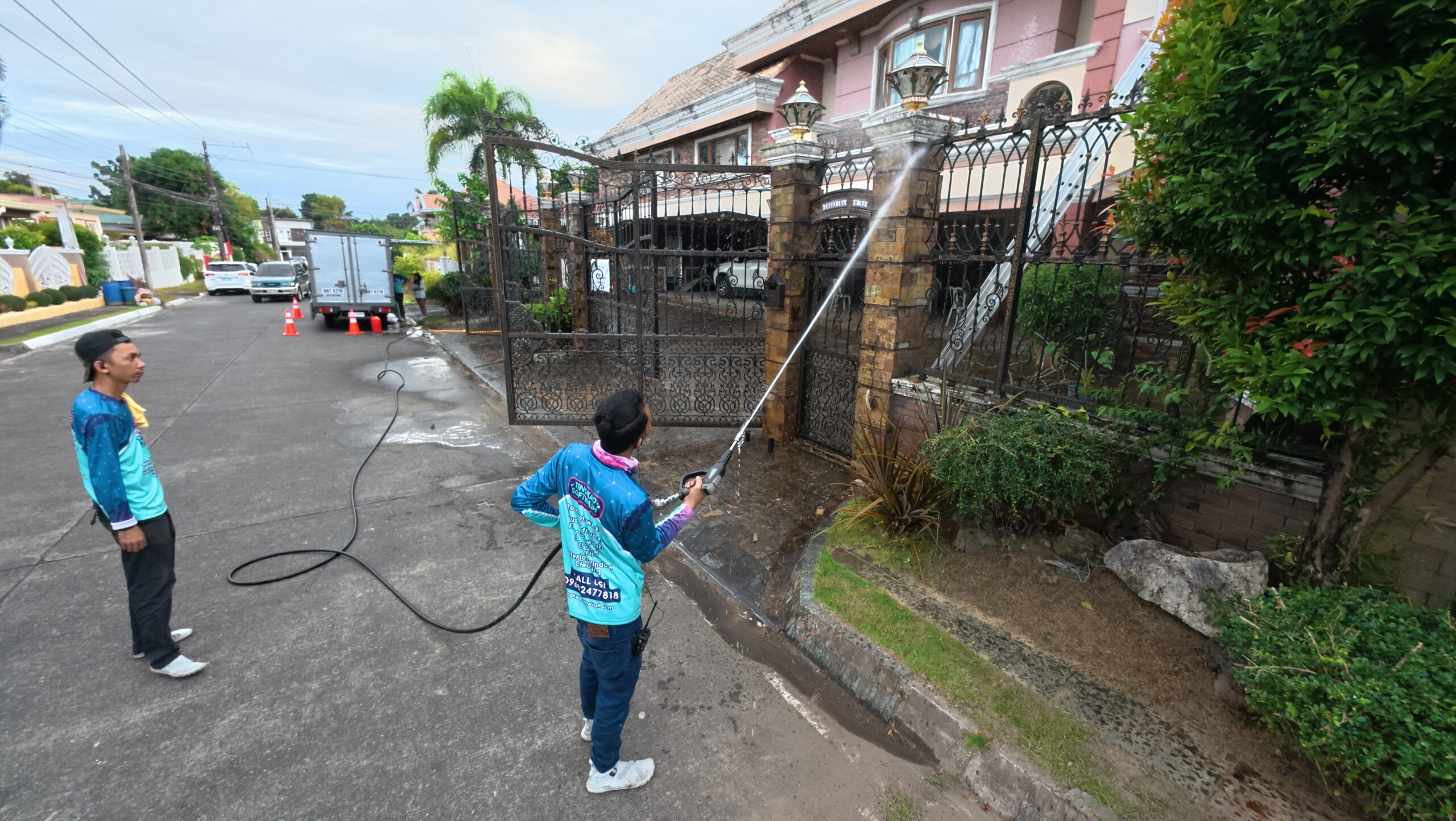 Technician soft washing a wall sidings and paved driveway entrance to remove mold and stains.