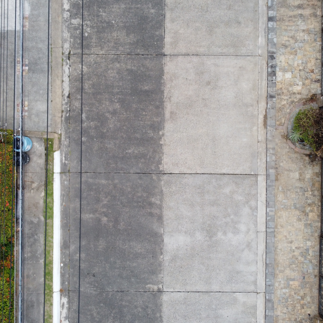 Top-down view of a concrete road half-cleaned, showing the dramatic difference between weathered pavement and restored concrete.