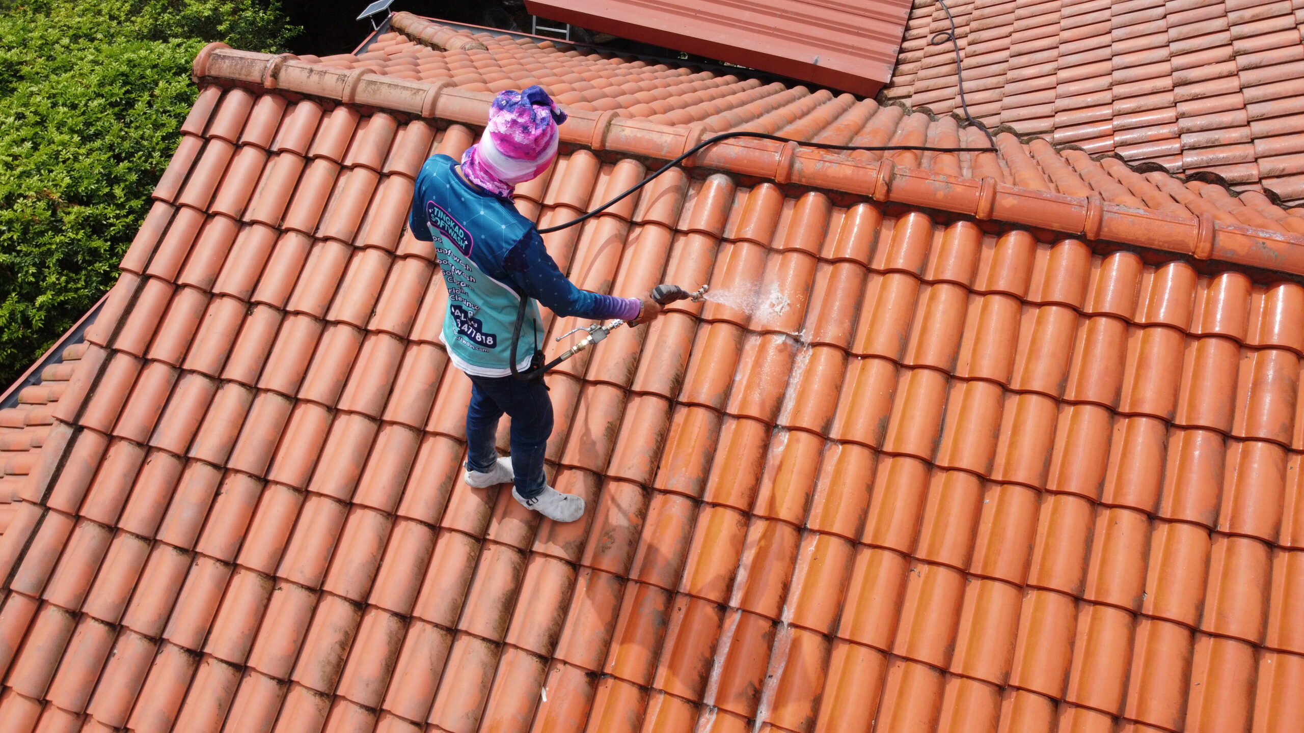 Professional roof cleaning service softwashing terracotta clay tiles to remove dark stains.
